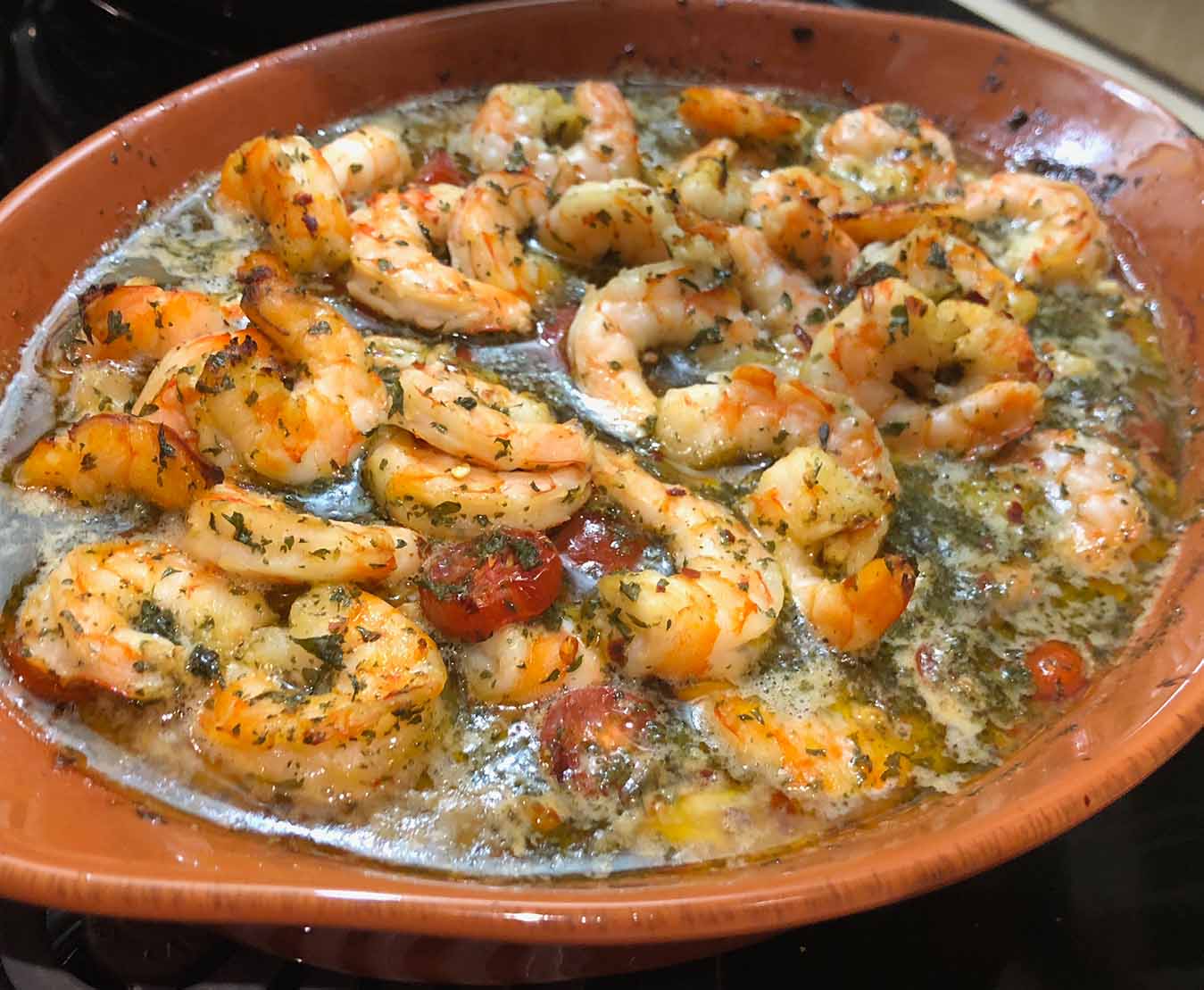 Spicy baked shrimp in garlic olive oil sauce with tomatoes and herbs.